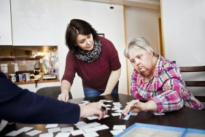Healthcare worker assisting women with down syndrome in arranging cards at table